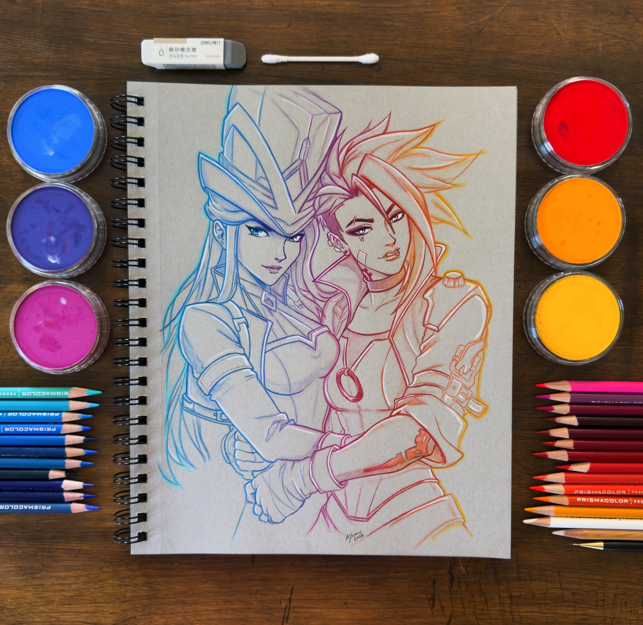 Colourful hand-drawn character artwork in a sketchbook, surrounded by pencils and pigments.